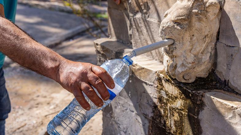 oseba toči vodo v plastenko pri vodnjaku