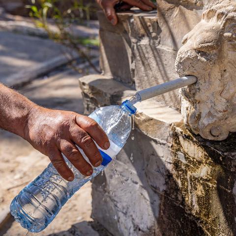 oseba toči vodo v plastenko pri vodnjaku