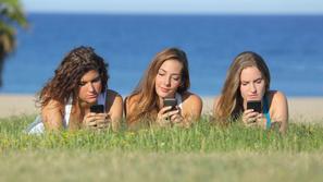Dekleta uporabljajo mobilni telefon na plaži