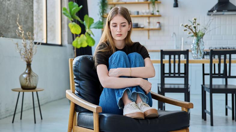 žalostna mlada ženska sedi na stolu v dnevni sobi