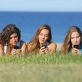 Dekleta uporabljajo mobilni telefon na plaži