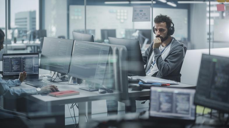 Moški programer v pisarni za računalnikom z zasloni