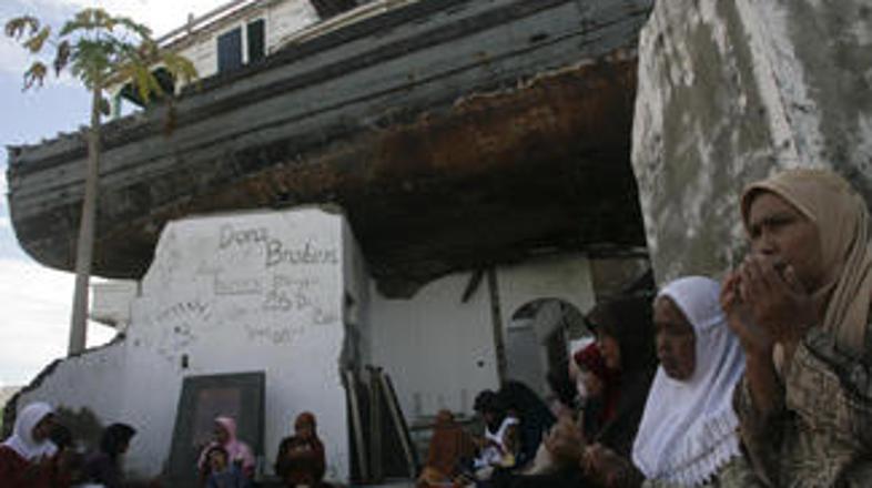 Ženske iz province Aceh molijo pod ladjico, ki jo je cunami odvrgel na hišo.