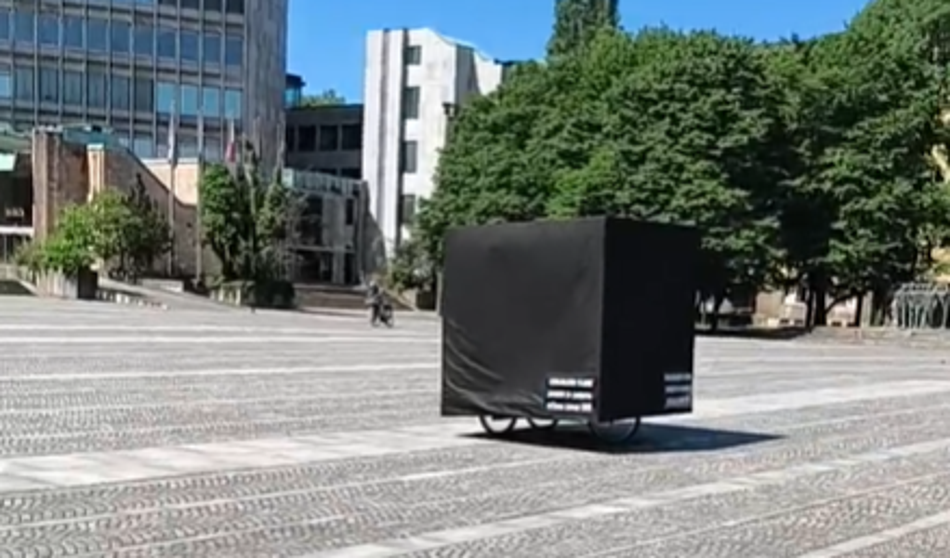 Na Trgu republike kolesari črna kocka, slišijo se besede ...