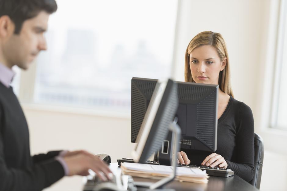 Moški in ženska sedita za mizo v pisarni in delata na računalniku | Avtor: Profimedia