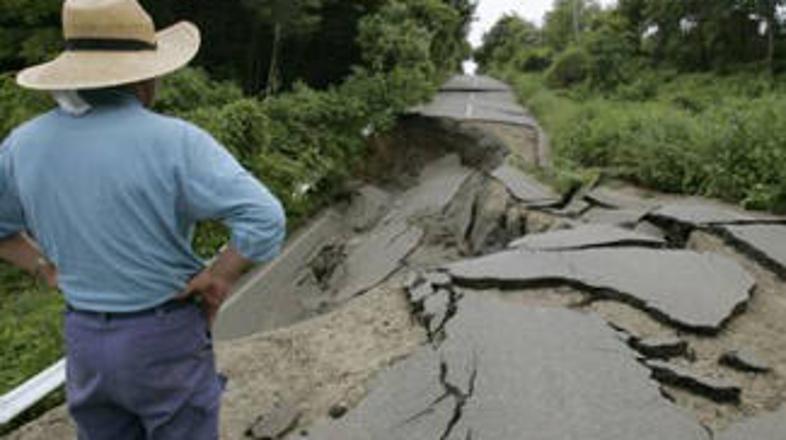 Prebivalec prizadetega območja si ogleduje škodo na cesti, ki jo je povzročil po