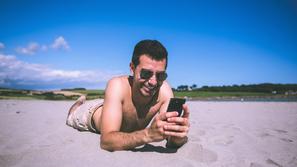 Moški uporablja mobilni telefon na plaži