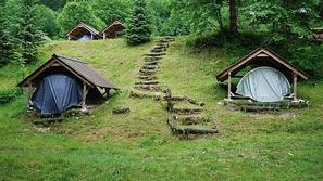 V leseni hiški šotor, v šotoru vzmetnica in odeja – soška postelja sredi neokrnj