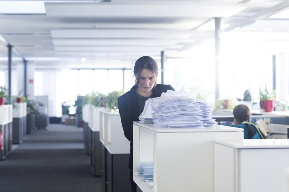 Ženska ima v rokah kup papirjev v pisarni | Avtor: Profimedia