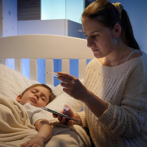mama meri vročino otroku, v rokah ima telefon