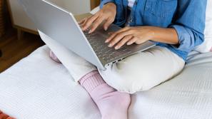 Ženska sedi na postelji z računalnikom v naročju