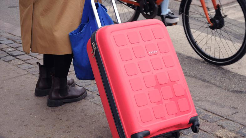 ženska s kovčkom stoji na pločniku