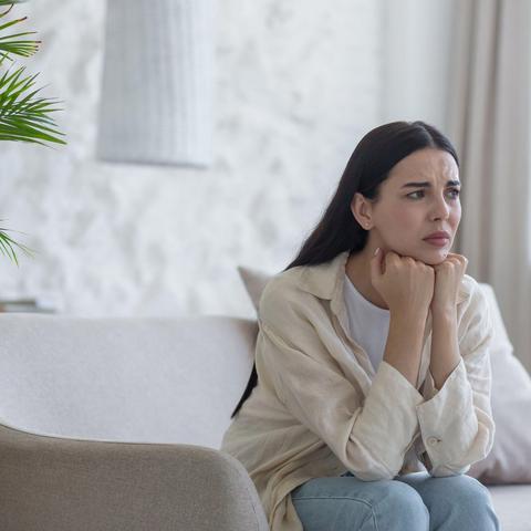 zaskrbljena ženska sedi na kavču v dnevni sobi