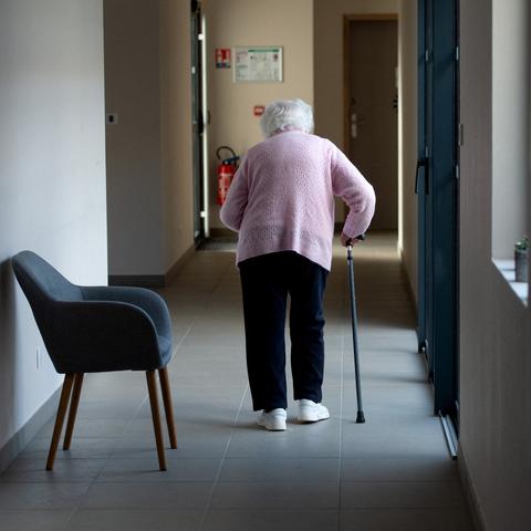 starejša ženska s palico hodi po hodniku v domu starejših občanov