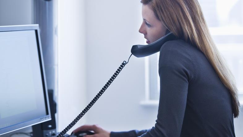 ženska v pisarni za računalnikom na telefonu