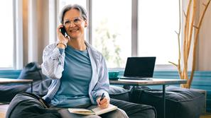 Starejša ženska telefoni in si piše v zvezek