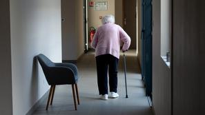 starejša ženska s palico hodi po hodniku v domu starejših občanov