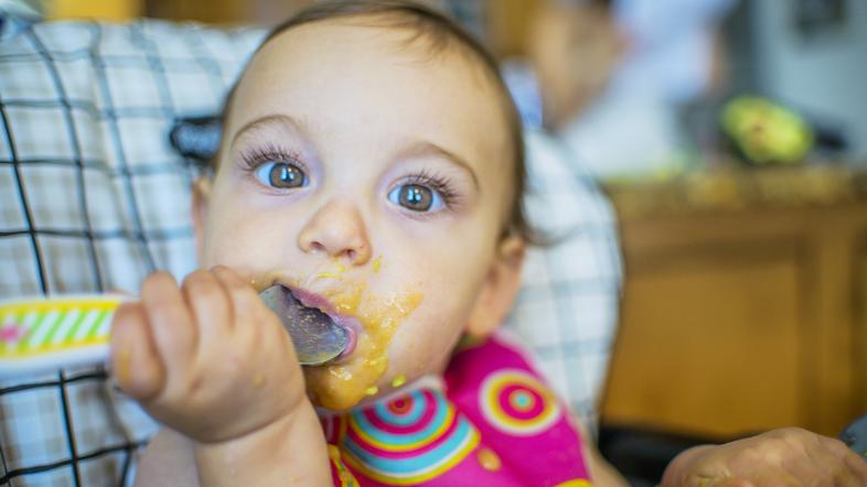 deklica sedi v stolčku in je pasirano hrano