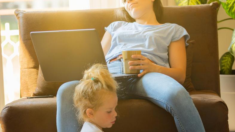 Utrujena ženska z otrokom dela na računalniku